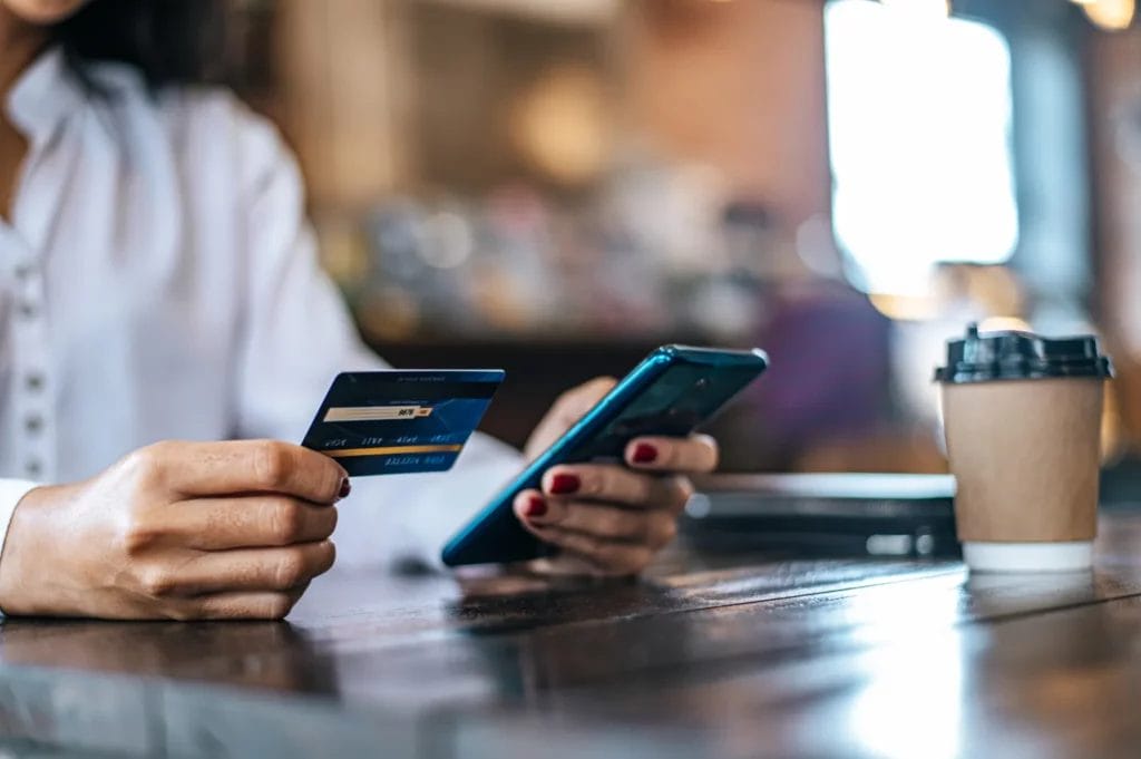 a woman holding credit card and phone for payment in cafe