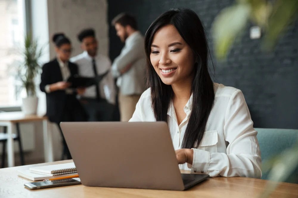 cheerful-young-asian-businesswoman-using-laptop